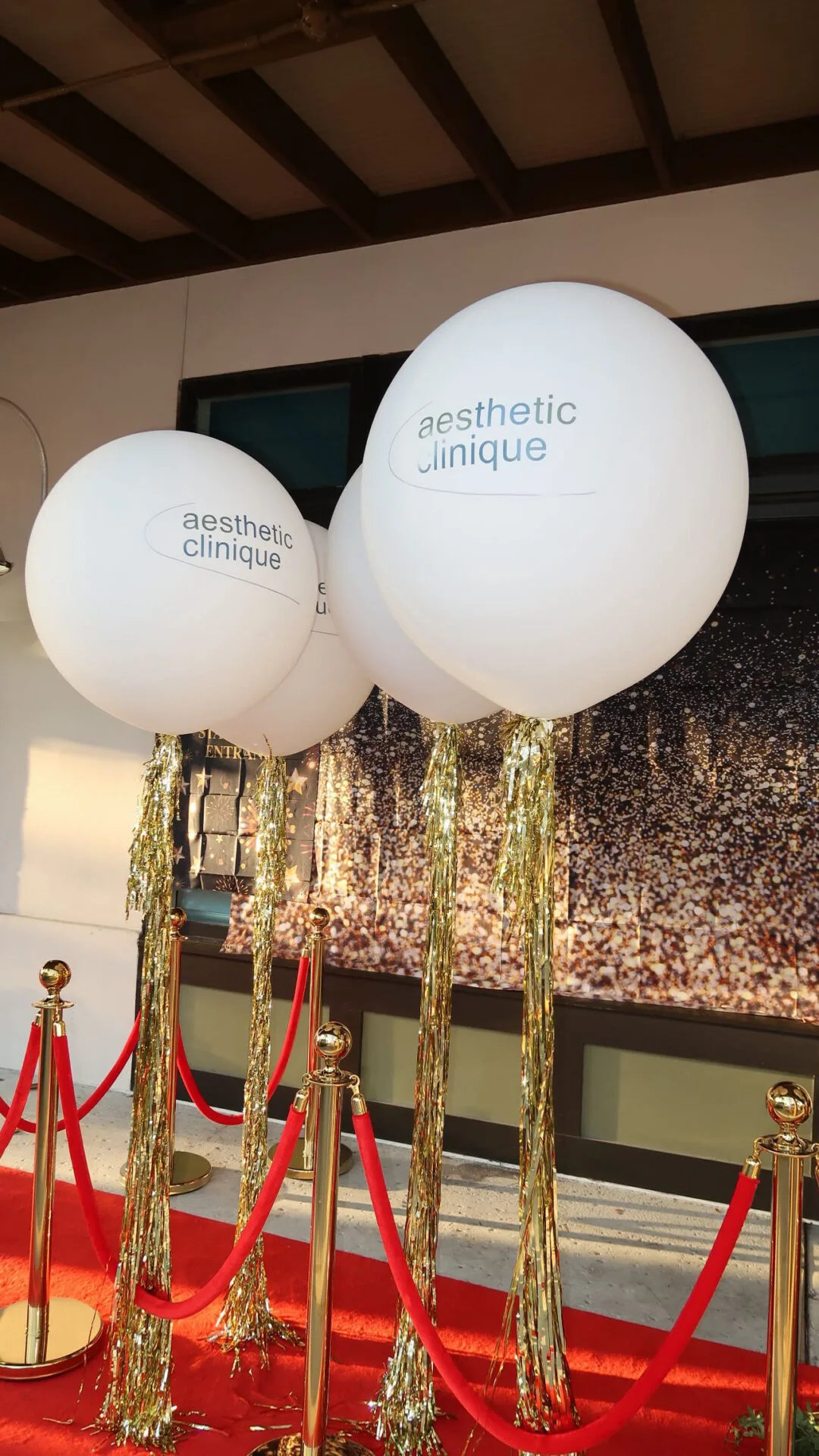 Branded Aesthetic Clinique balloons, gold tassels and red carpet at the entrance to a previous open house